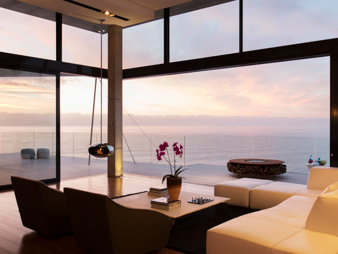 Elegant interior of a seaside luxury home with panoramic ocean view at dusk, featuring modern furniture and fireplace